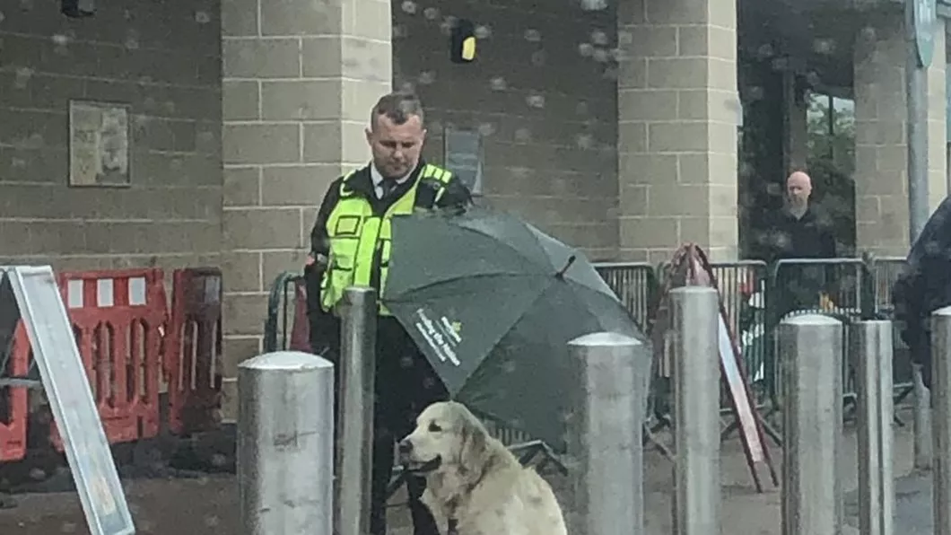 Eroii există Un agent de pază îi ţine umbrela unui câine pentru a nu se uda