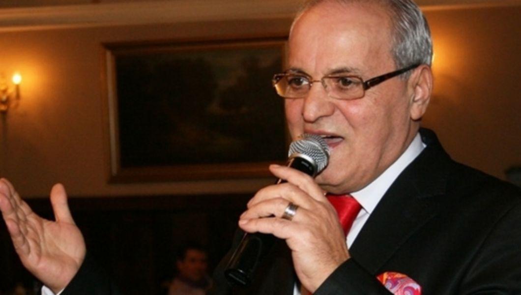 Nelu Ploieșteanu imbracat la costum cu cravata rosie si batista canta la microfon
