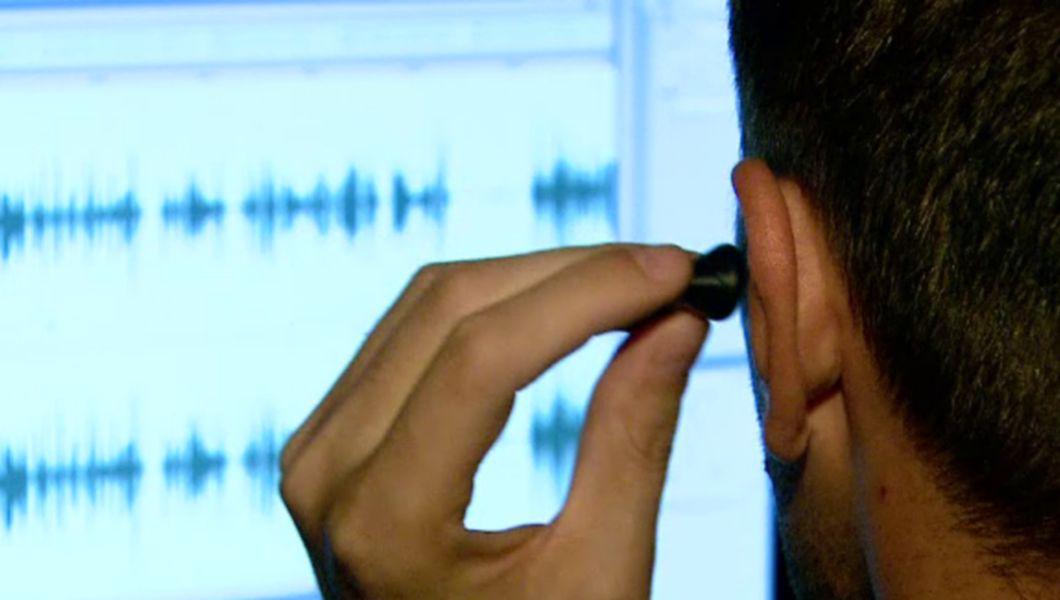 un bărbat își introduce o cască în ureche și ascultă convorbirile - imagine din spate