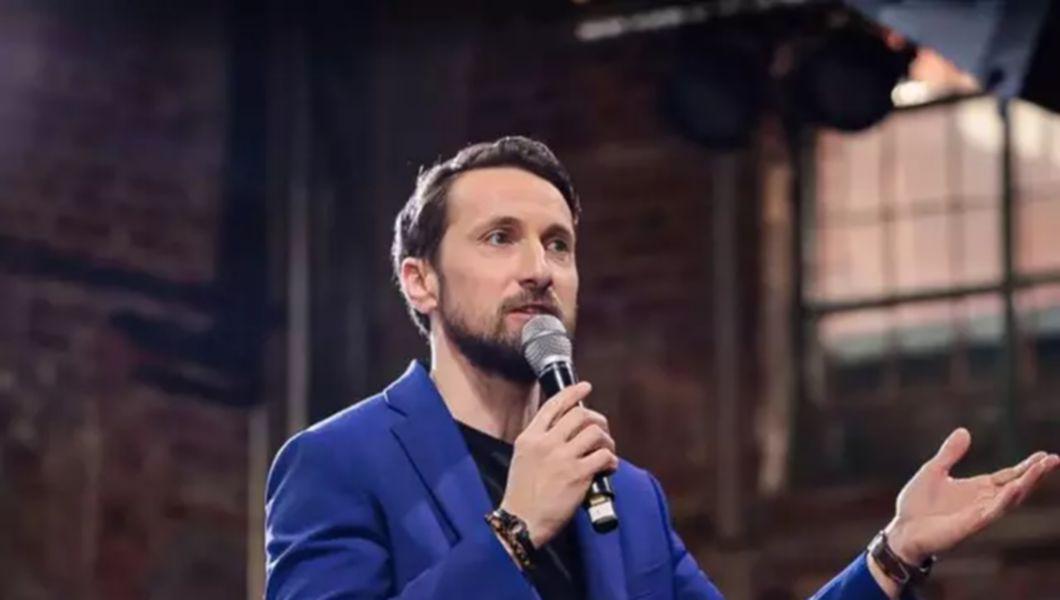 Dani Oțol îmbrăcat cu un costum albastru și ține un microfon în mână