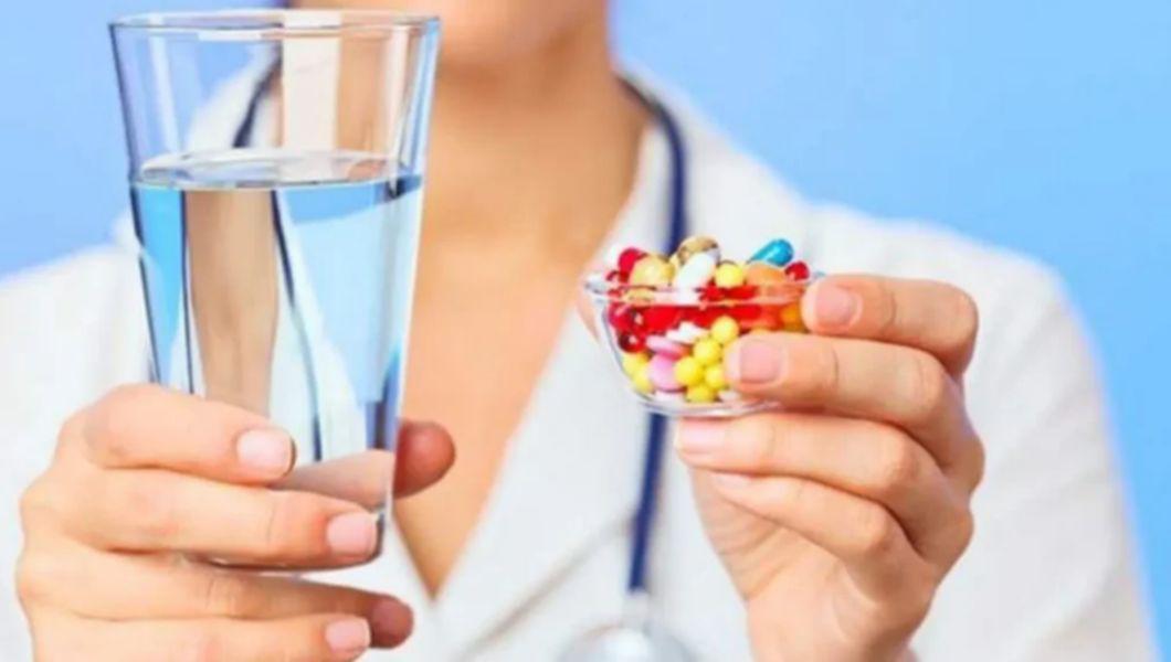 medic care tine in mana un pahar cu apa si in alta mana un recipient cu antibiotice