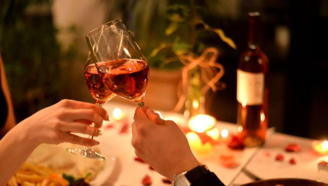 doua persoane ce ciocnesc doua pahare de vin la o cina romantica