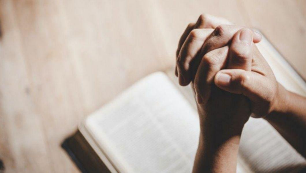 mâini împreunate care se roagă în fața unei cărți