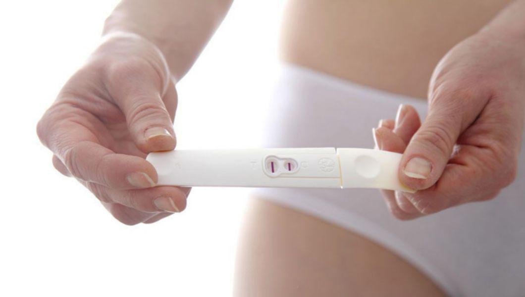 femeie care tine un test de sarcina pozitiv in mana