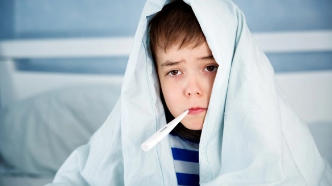 un copil cu febră și cu un termometru în gură