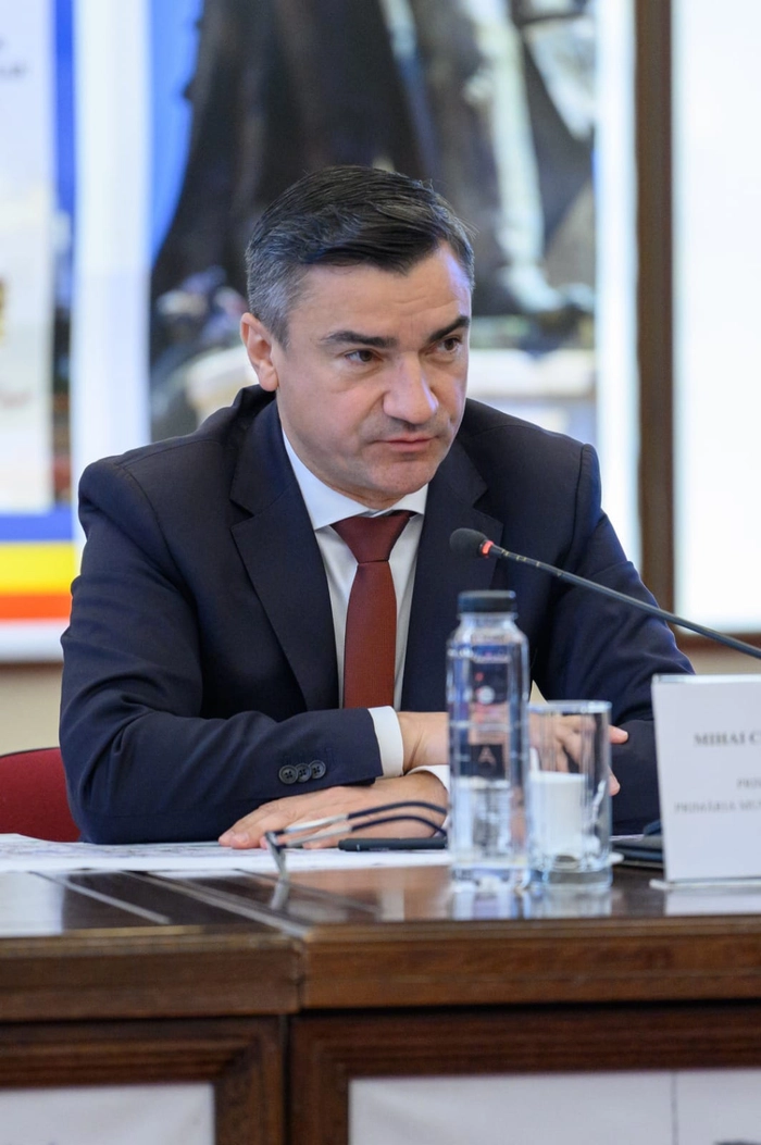 Mihai Chirica in costum negru da declaratii la o masa
