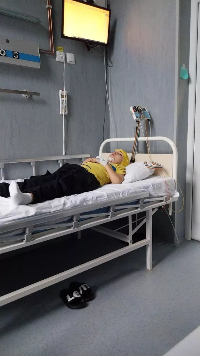 Baietelul doarme intr-un pat, invelit cu o patura, cu o caciulita in cap si conectat la aparate