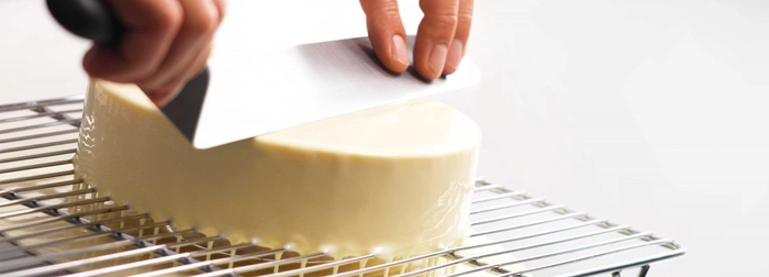 persoana care aplica glazura alba de ciocolata pe tort