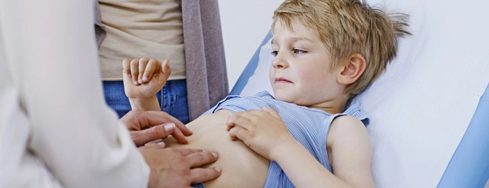 medic care apasa pe burta unui copil culcat pe un pat de spital