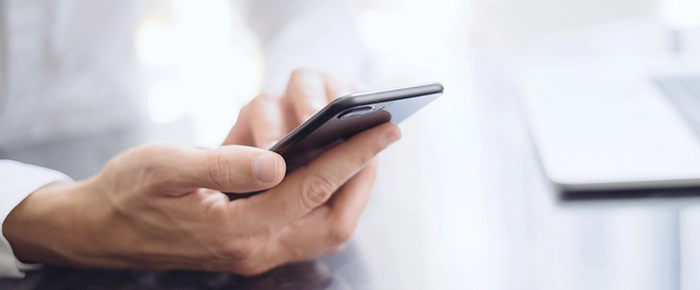 persoana care tine un telefon in mana si tasteaza un text