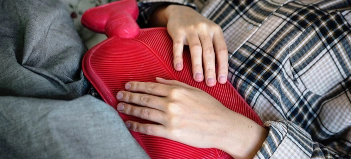 persoana care tine o perna cu apa fierbinte pe abdomen