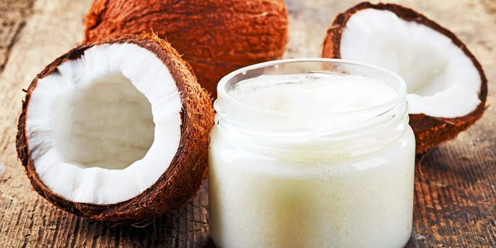 ulei de cocos si nuca de cocos sectionata prezentate pe un suport de lemn 