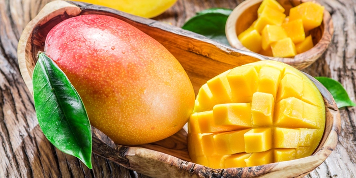 un mango intreg si unul taiat intr-un vas din lemn