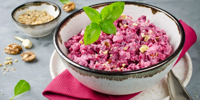 un bol cu salata pe o masa langa un bol mai micut cu condimente si tacamuri