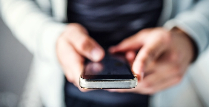 persoana care tine un telefon in mana si tasteaza un text