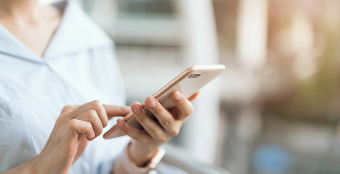 persoana care tine un telefon in mana si tasteaza un text