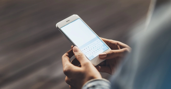 persoana care tine un telefon in mana si tasteaza un text