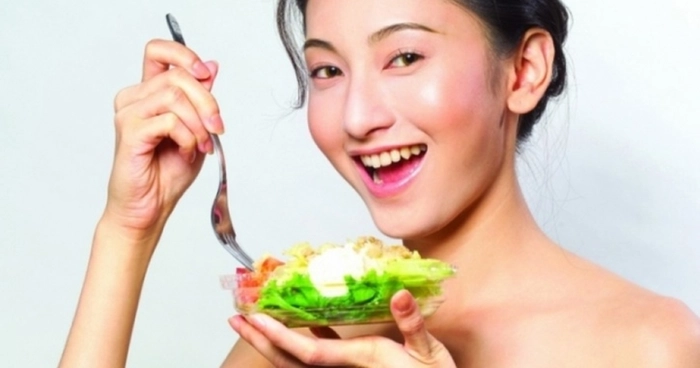 femeie care mananca tine un bol cu salata si zambeste