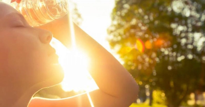 femeie care tine o sticla de apa pe frunte stand afara in soare