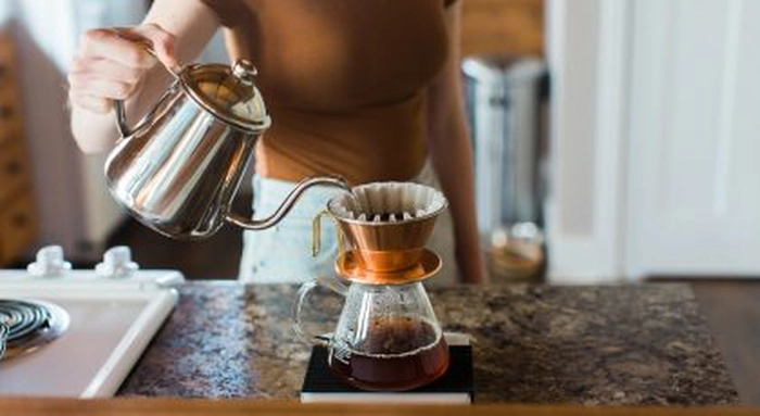 femeie care toarna apa peste cafeaua din filtrul de hartie