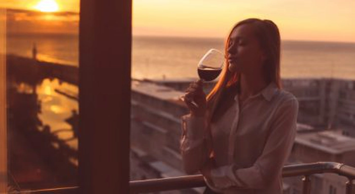 fata care bea vin in balcon, la apus de soare, dupa munca de acasa