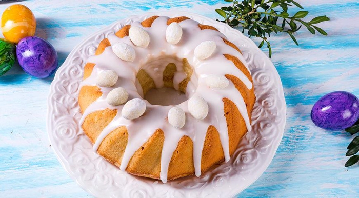 un cozonac cu ciocolata topita desupra langa mai multe oua vopsite pentru paste