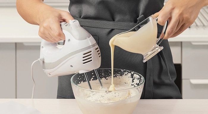 femeie care pregateste cu ajutorul unui mixer crema cu lapte condensat