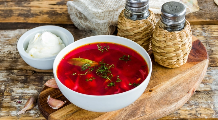 un bol cu ciorba de legume pe o masa langa mai multe condimente