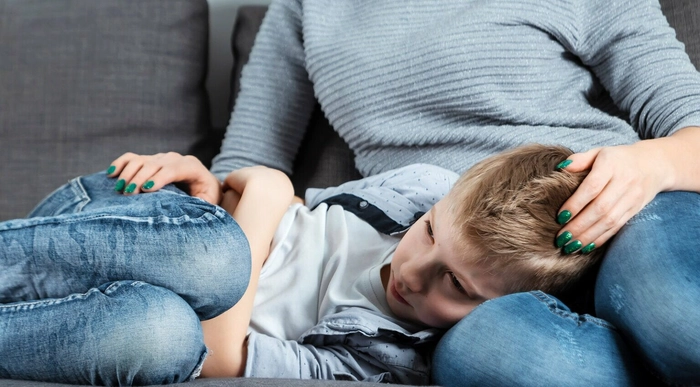 copil care sta culcat pe picioarele unei persoane si se tine de burta din cauza durerii