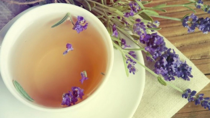 o cana de ceai ce are flori de lavanda in ceai si langa cana pe o masa
