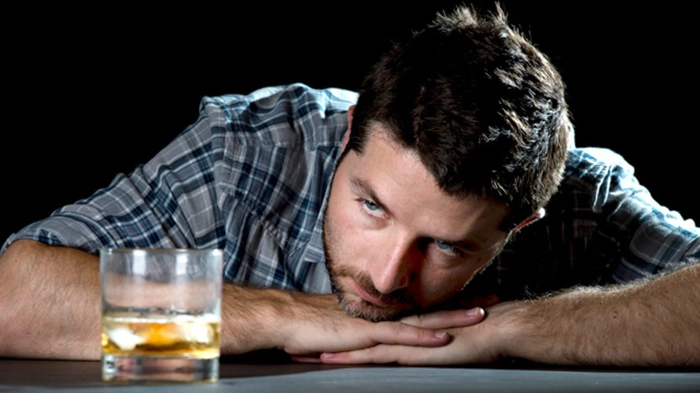 barbat care priveste ingandurat un pahar cu alcool