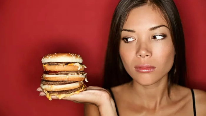 femeie care priveste un burger in timp ce il tine in mana 