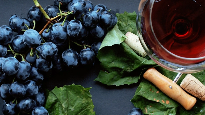 strugure alaturi de un dop de pluta, un desfacator de vin si un pahar plin pe o masa