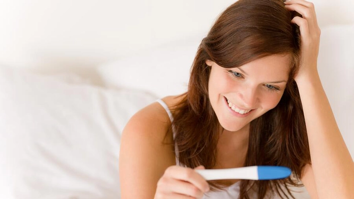 femeie care priveste un test de sarcina si zambeste