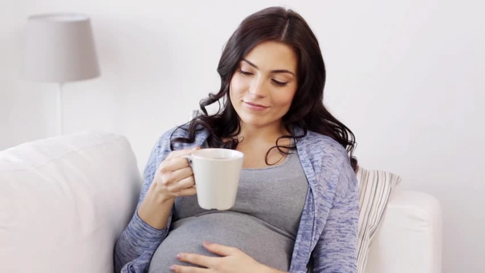femeie insarcinata care tine o cana de ceai in mana