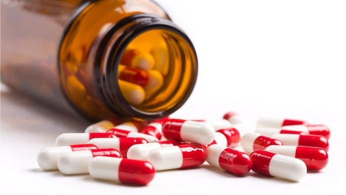 un recipient închis la culoare și câteva antibiotice vărsate