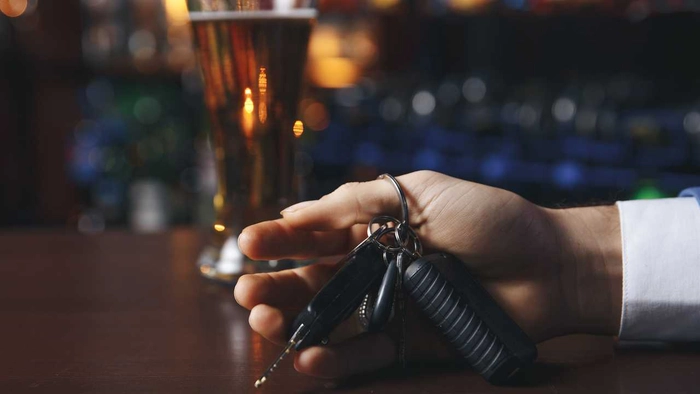  o persoana cu chei in mana si un pahar de alcool pe fundal