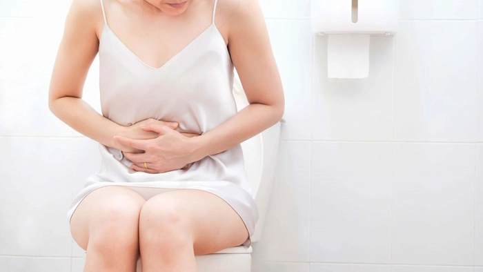 femeie care sta pe veceu si se tine de abdomen