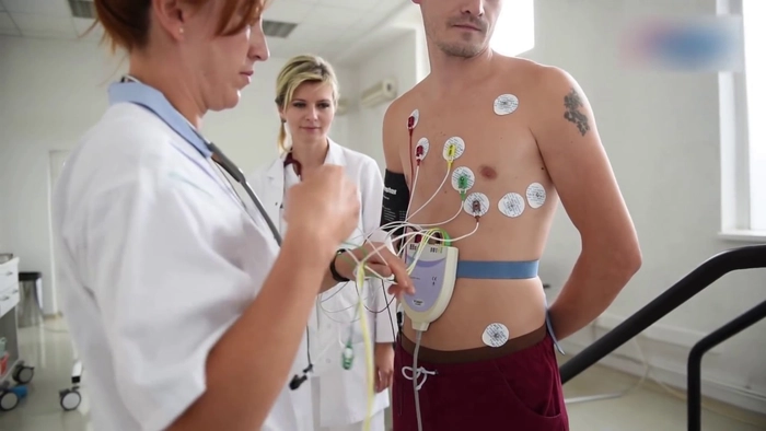 doua asistente care aplica unui barbat pe piept instrumentul pentru a efectua cardiograma