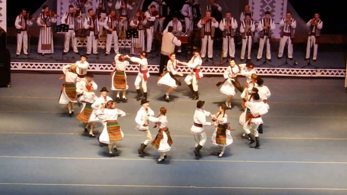 oameni imbracati in costum popular jucand hora
