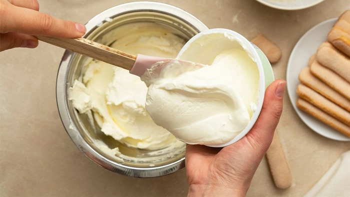 persoana care adauga crema de mascarpone intr-un bol aflat pe masa