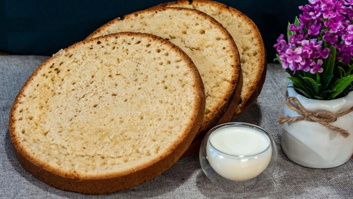 pandispan taiat in mai multe bucati langa un pahar cu lapte si flori