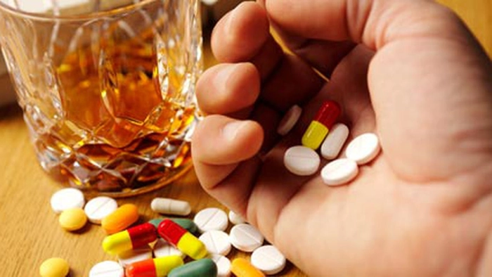 barbat care tine in mana mai multe pastile si are alaturi un pahar cu alcool