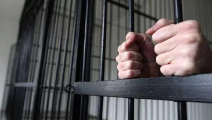 barbat incarcerat ce se tine cu mainile de bare