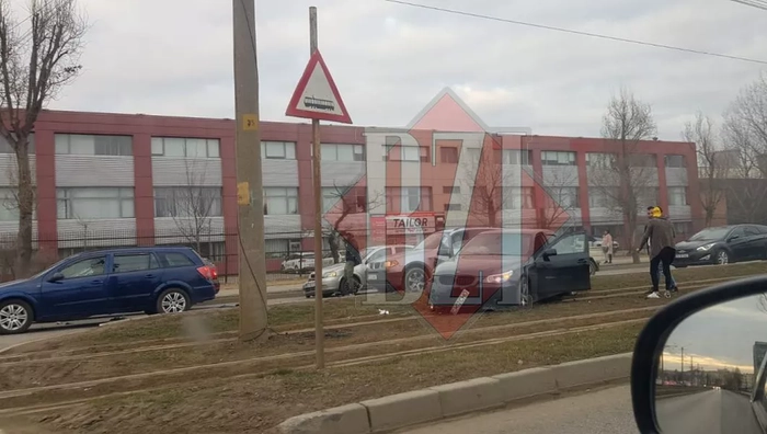 Mai multe autoturisme pe o strada, accident rutier, pe fundal o cladire gri cu rosu