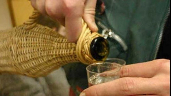 o persoană toarnă țuică într-un pahar mic