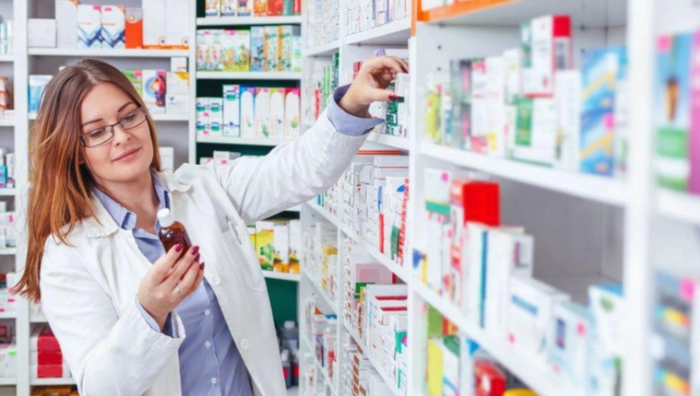 farmacist analizeaza un flacon in fata unui raft de farmacie plin