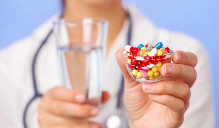 medic care intinde un recipient cu antibiotice si tine un pahar cu apa in mana
