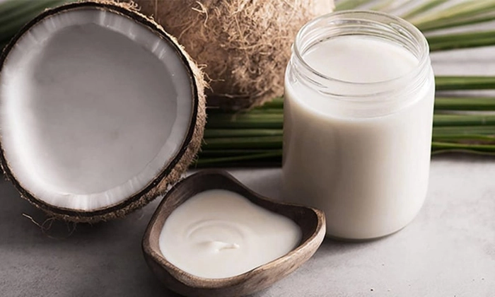 ulei de cocos si nuca de cocos taiata pe un  suport de lemn 
