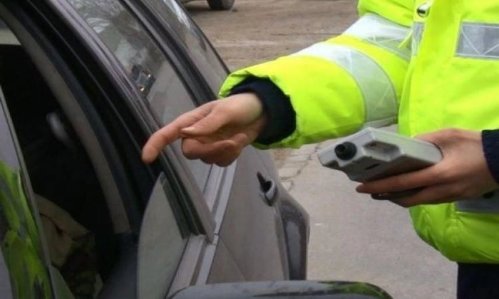 o persoana imbracata in uniforma reflectorizanta, cu un aparat alcooltest intr-o mana si cu o alta mana intinsa catre geamul deschis al unui automobil